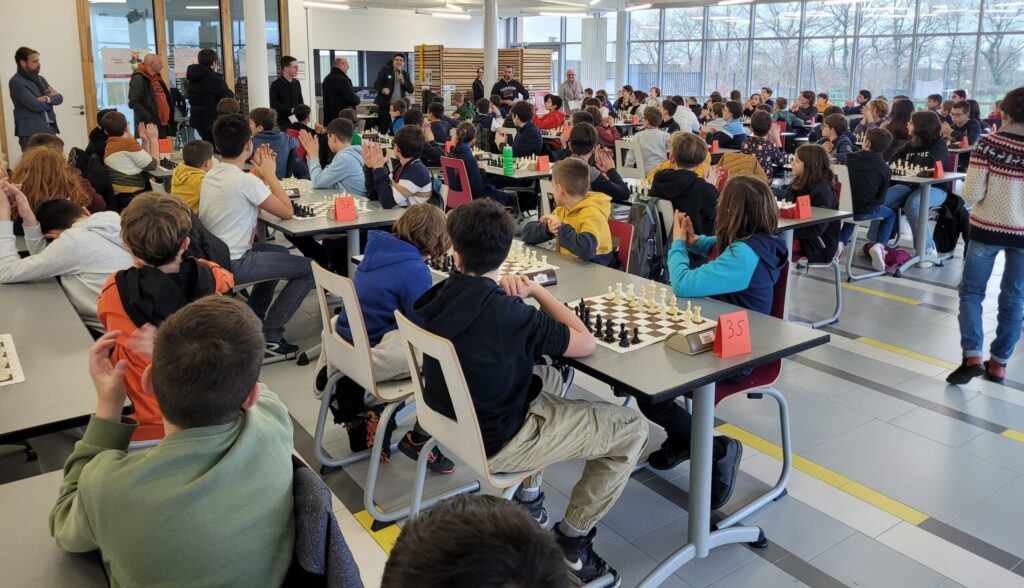 Salle remplie d'élèves participant à un tournoi d'échecs, avec des échiquiers sur les tables. 